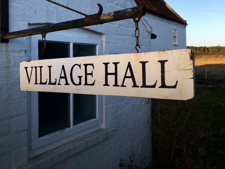 An old fashioned village hall sign swinging outside a white washed building